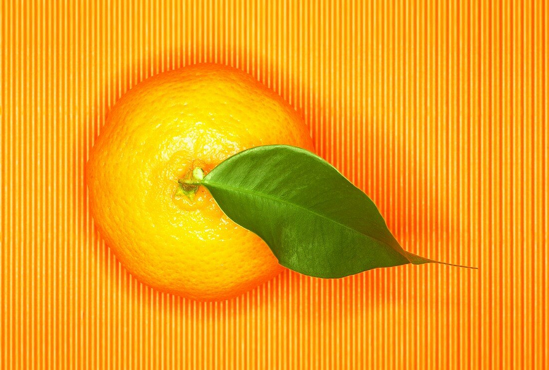 Eine Mandarine mit Blatt auf orangefarbenem Untergrund