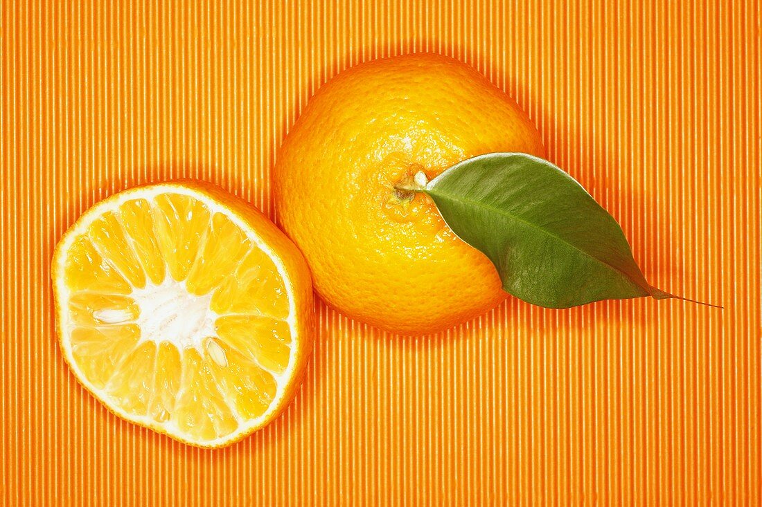 Mandarine und Mandarinenhälfte auf orangefarbenem Untergrund