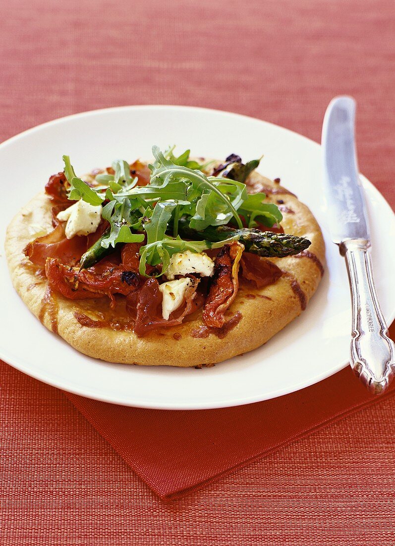 Mini-pizza with dried tomatoes, prosciutto and rocket