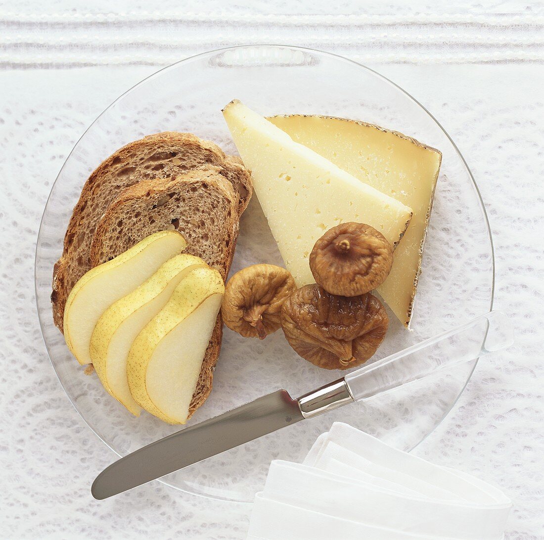 Cheese, dried figs, bread and pear on plate
