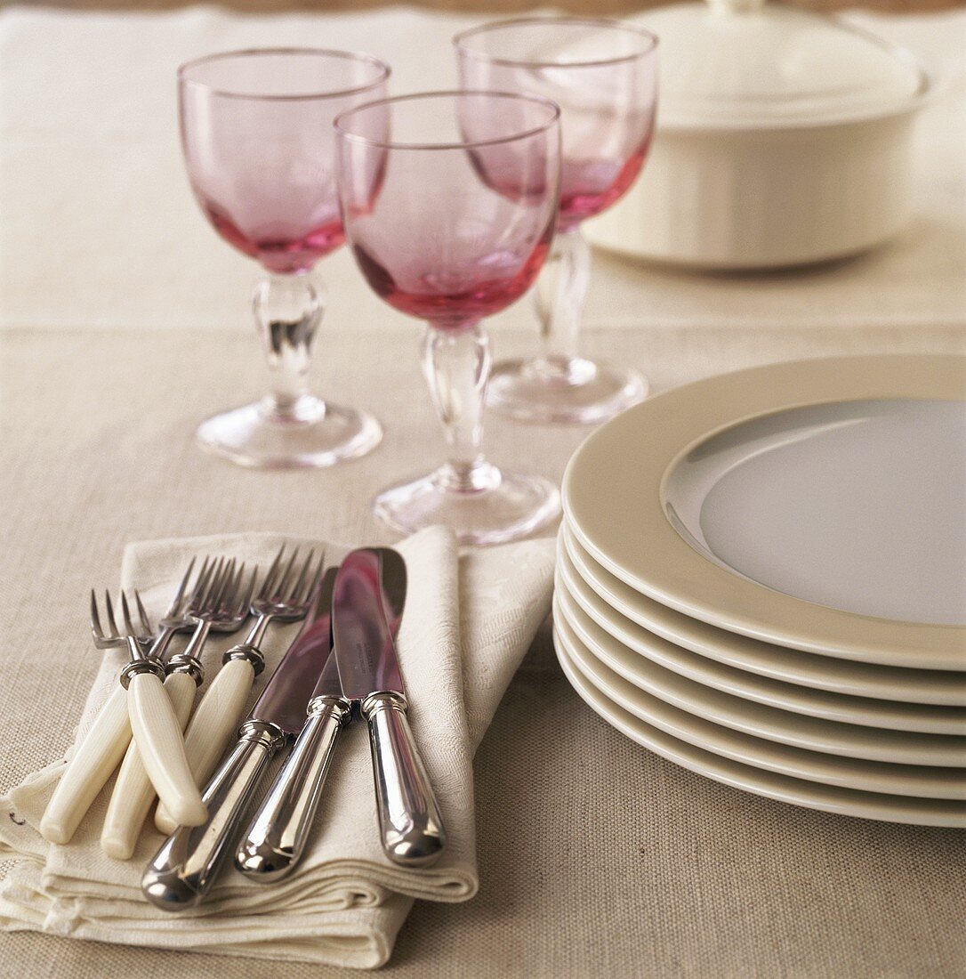 Cutlery, pile of plates and wine glasses