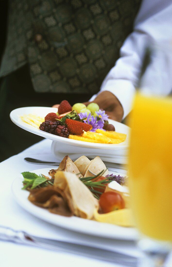 Breakfast table with plate of cold cuts & plate of fruit