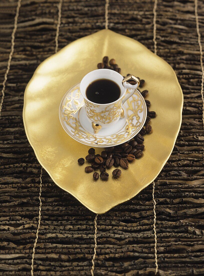 A cup of espresso on a gold tray with coffee beans