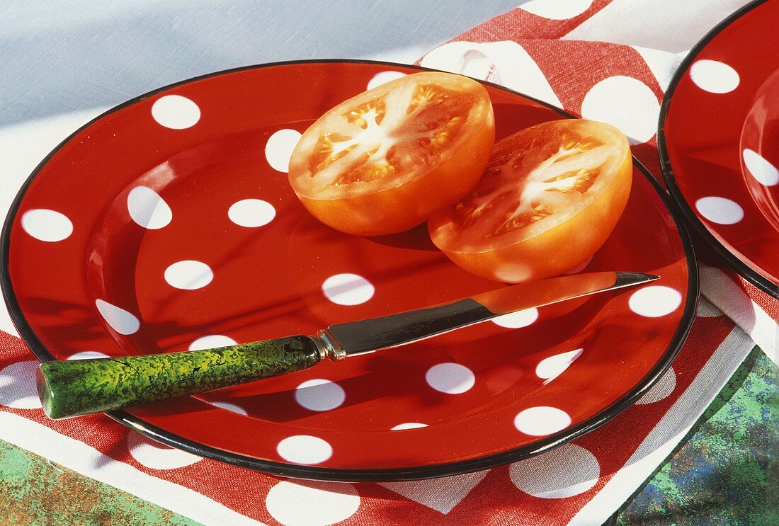 Halved tomato with knife on spotted plate