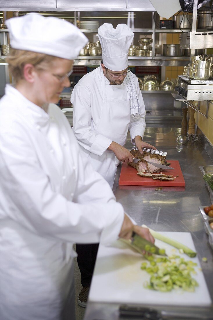 Chefs carving meat and chopping vegetables