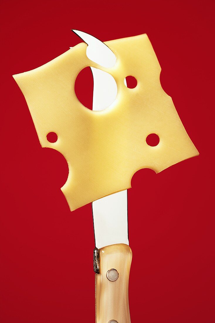 A slice of Emmental cheese hanging on a cheese knife