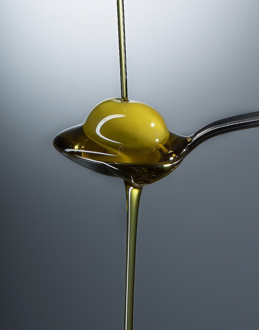 Ölivenöl fliesst über Löffel mit Olive