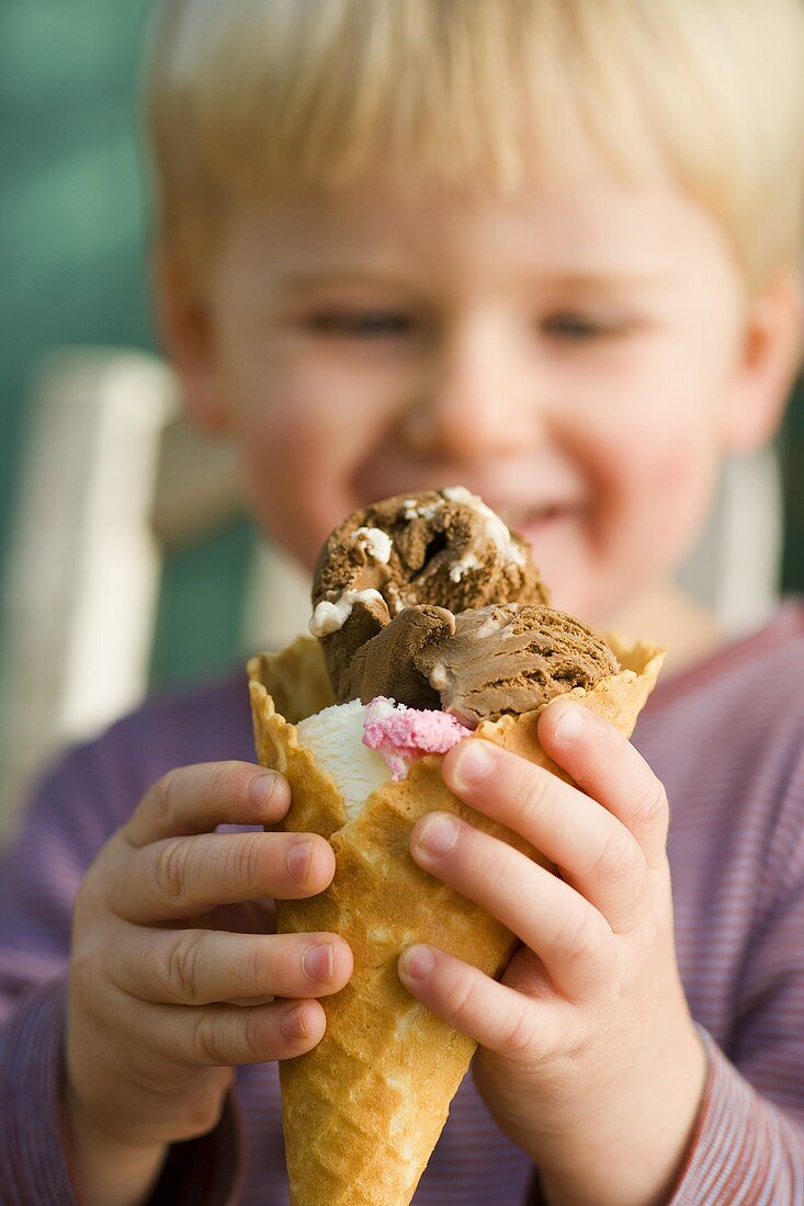 Kleiner Junge hält eine Waffeltüte mit gemischtem Eis