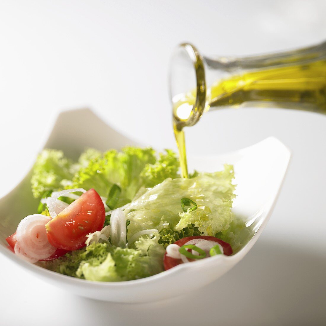 Pouring olive oil over salad leaves with tomatoes