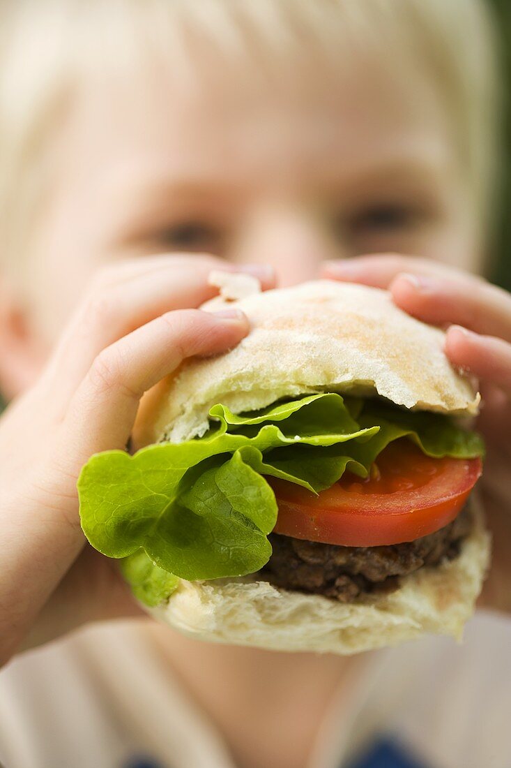 A little boy eating a burger with tomato and lettuce