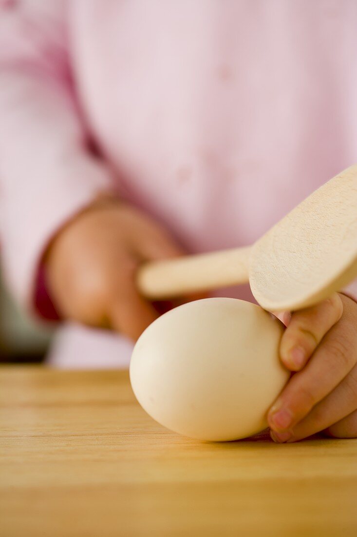 Kleine Mädchenhände halten einen Holzkochlöffel und ein Ei
