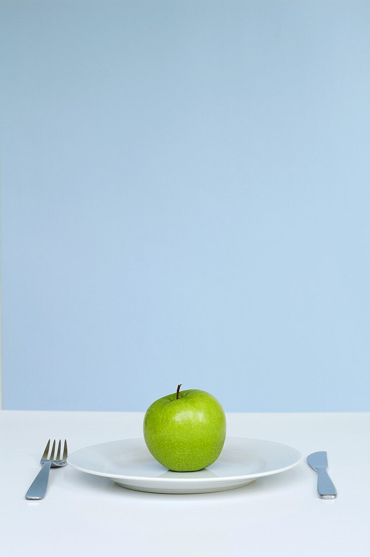 An apple on a plate with knife and fork