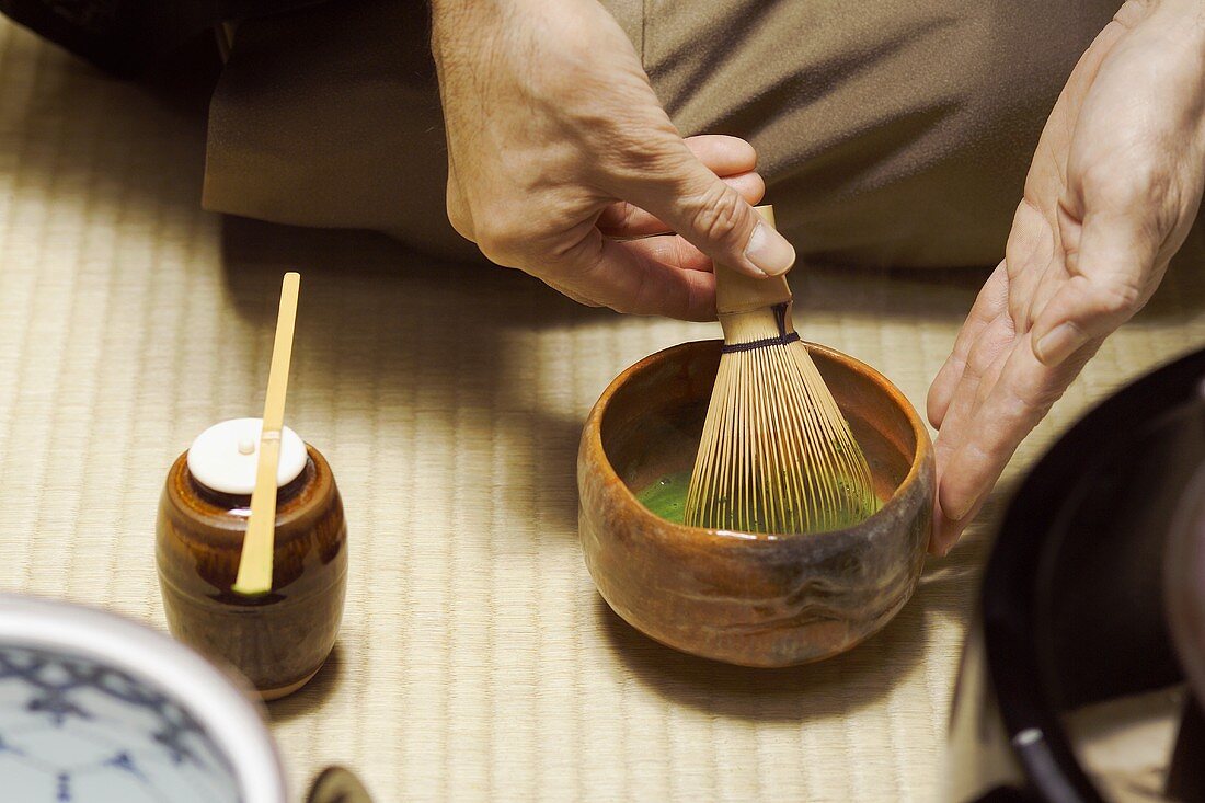 Tea master at tea ceremony, stirring tea with tea whisk