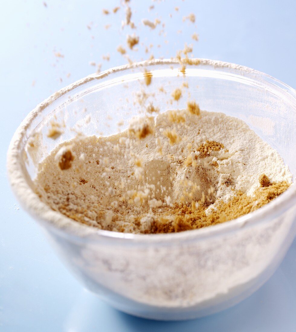 Sprinkling brown sugar onto flour in a glass bowl
