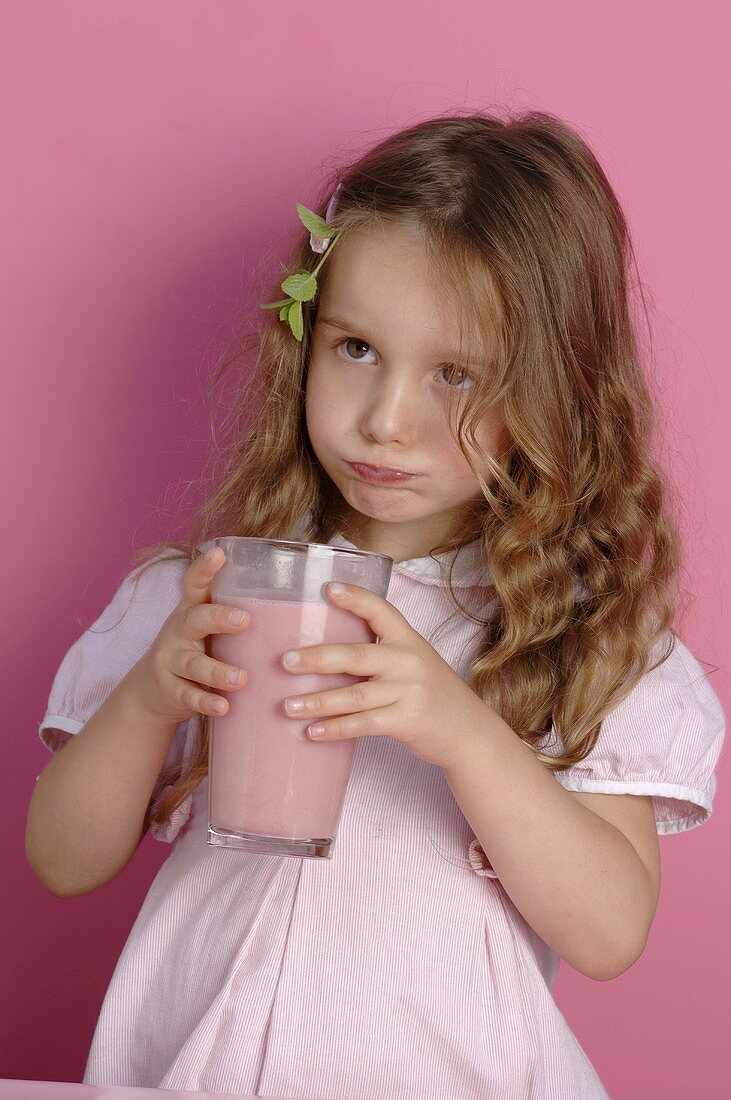 Kleines Mädchen hält ein Glas Erdbeermilch in den Händen