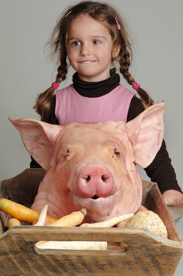 Pig's head and vegetables on tray, girl standing behind