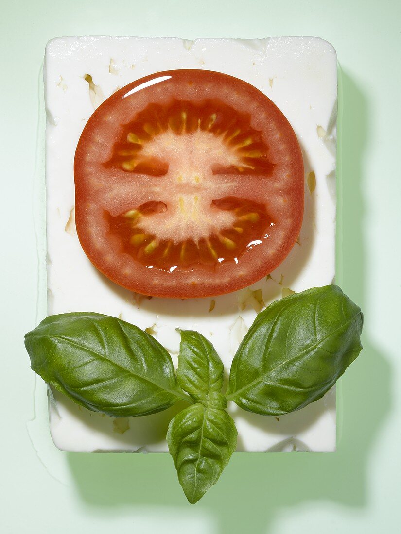 A slice of tomato with basil on a slice of feta