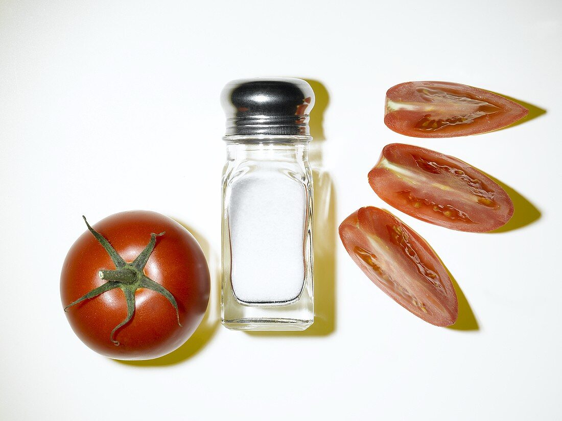 Whole tomato with salt shaker and three tomato wedges