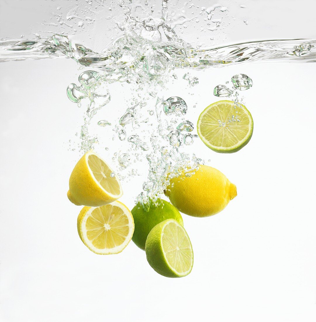 Zitronen und Limettenhälften fallen ins Wasser