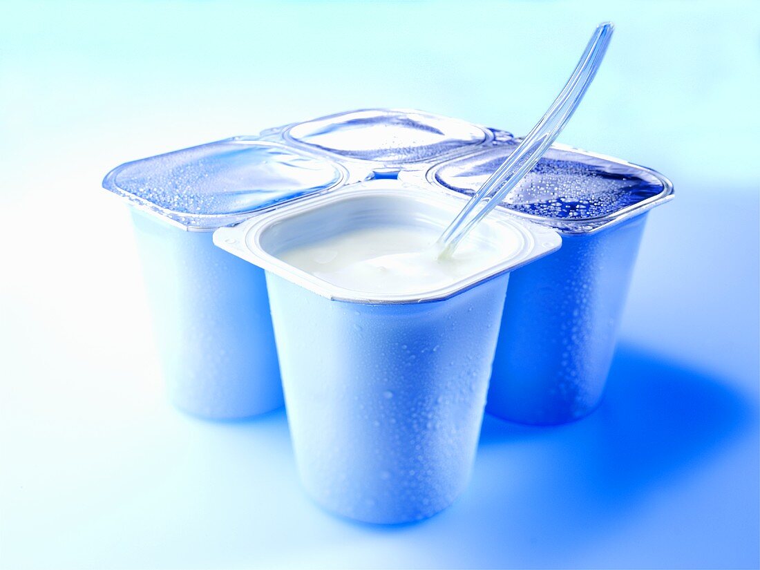 Four yoghurt pots, one open with spoon