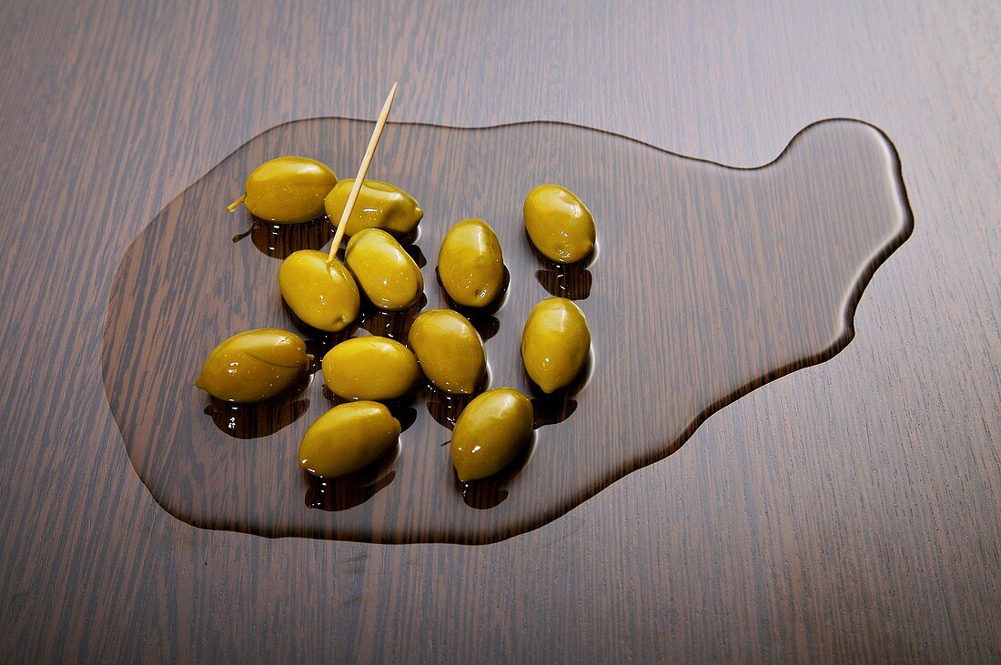 Grüne Oliven in Olivenöl auf einer Holzplatte