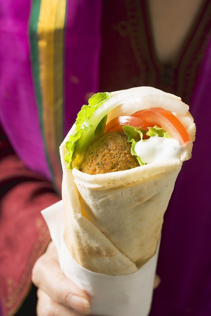 Person holding wrap filled with falafel (chick-pea balls)