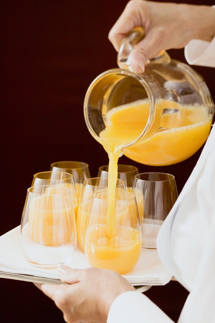 Zimmermädchen giesst Orangensaft in Glas
