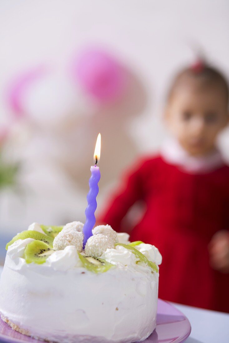 Kleine Kokos-Kiwi-Torte mit einer Kerze, Kind im Hintergrund