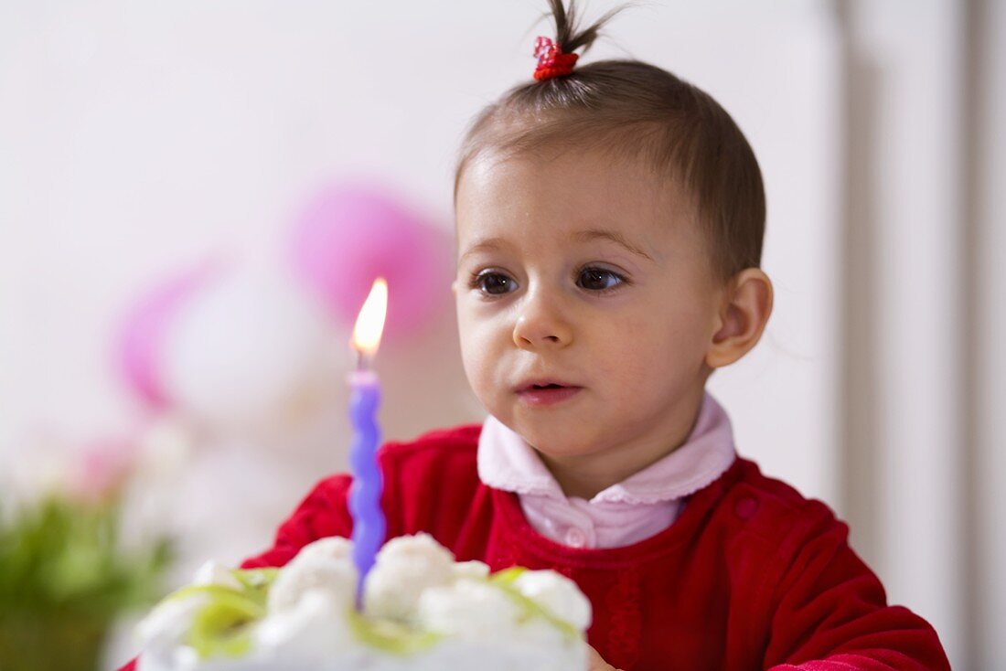 Kleines Mädchen bläst Kerze auf Kokos-Kiwi-Torte aus