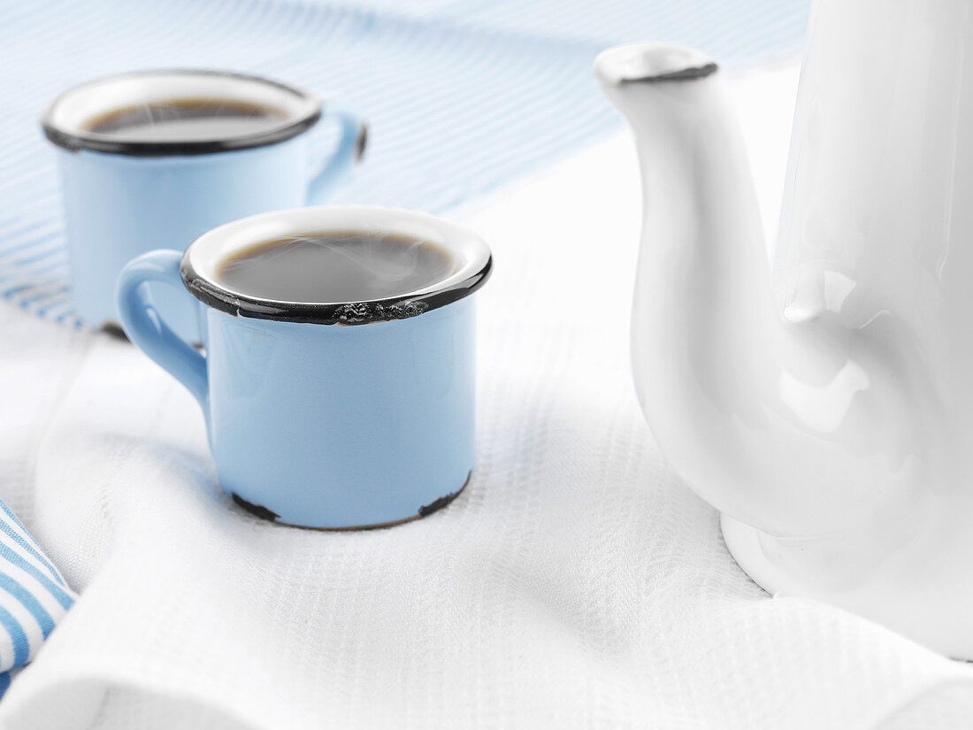 Coffee in blue cups beside white coffee pot
