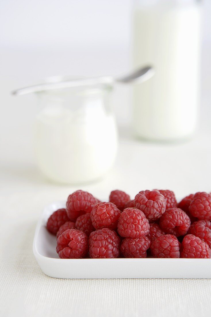 Fresh raspberries, jar of yoghurt in background
