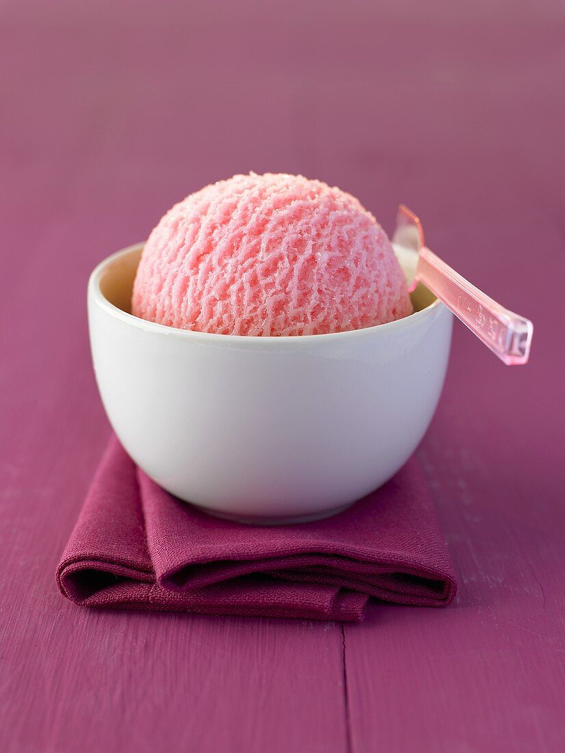 A scoop of raspberry ice cream in a bowl with plastic spoon