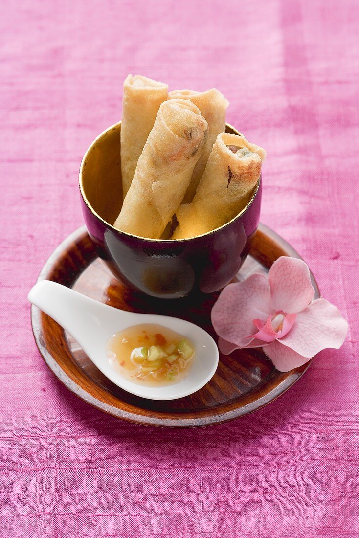 Spring rolls in lacquer bowl, dip on spoon, orchid