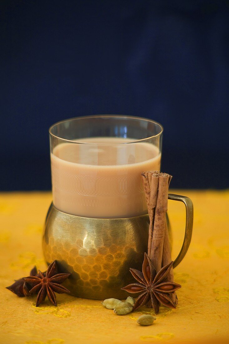 A glass of chai tea surrounded by spices