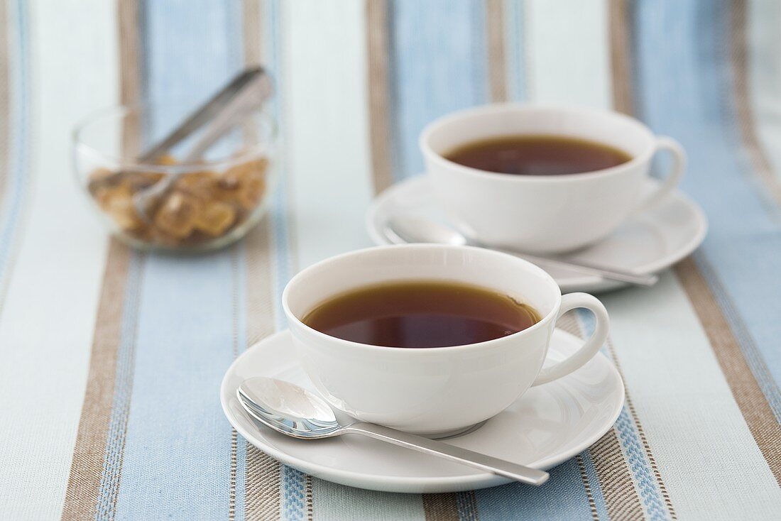 Two cups of black tea, sugar crystals in glass bowl