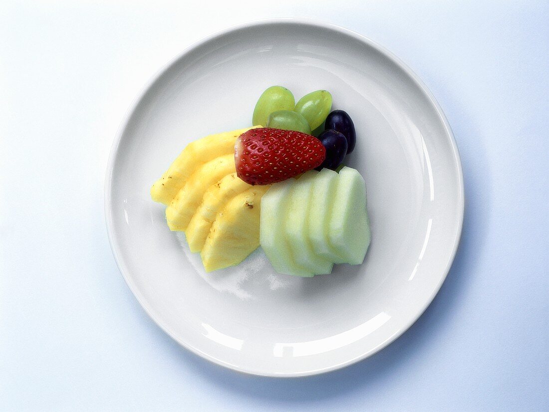 Apple and pineapple slices, grapes and strawberry on plate