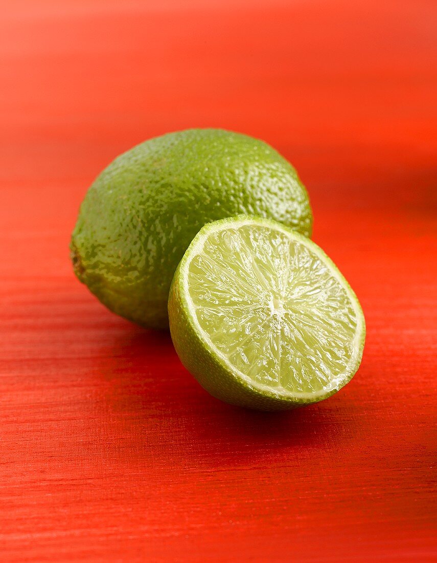 Whole and half lime on red background