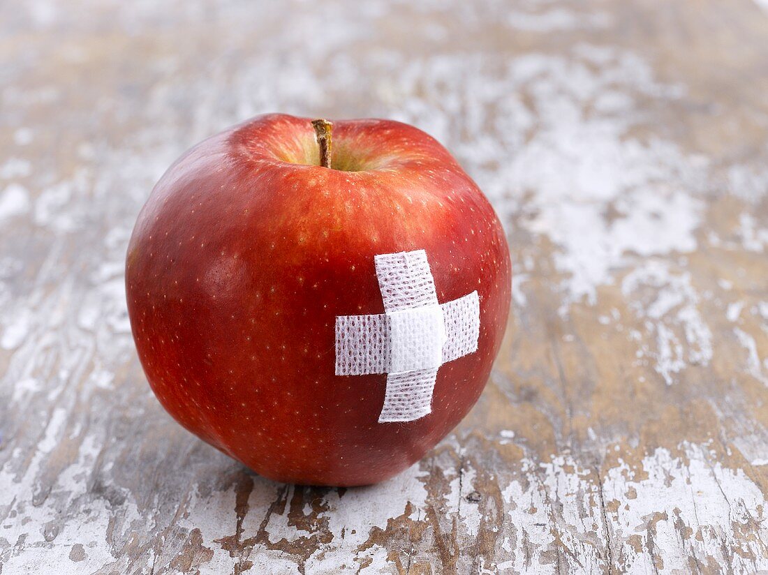 Ein roter Apfel mit Pflaster als Kreuz