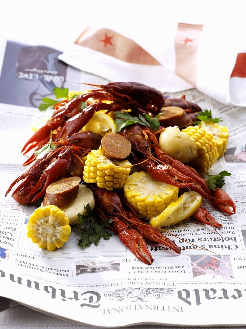 Freshwater crayfish with cobs of corn & sausage on newspaper