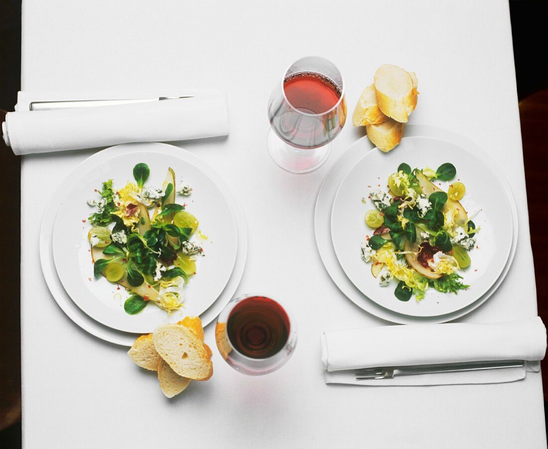 Two place-settings with salad, bread and red wine
