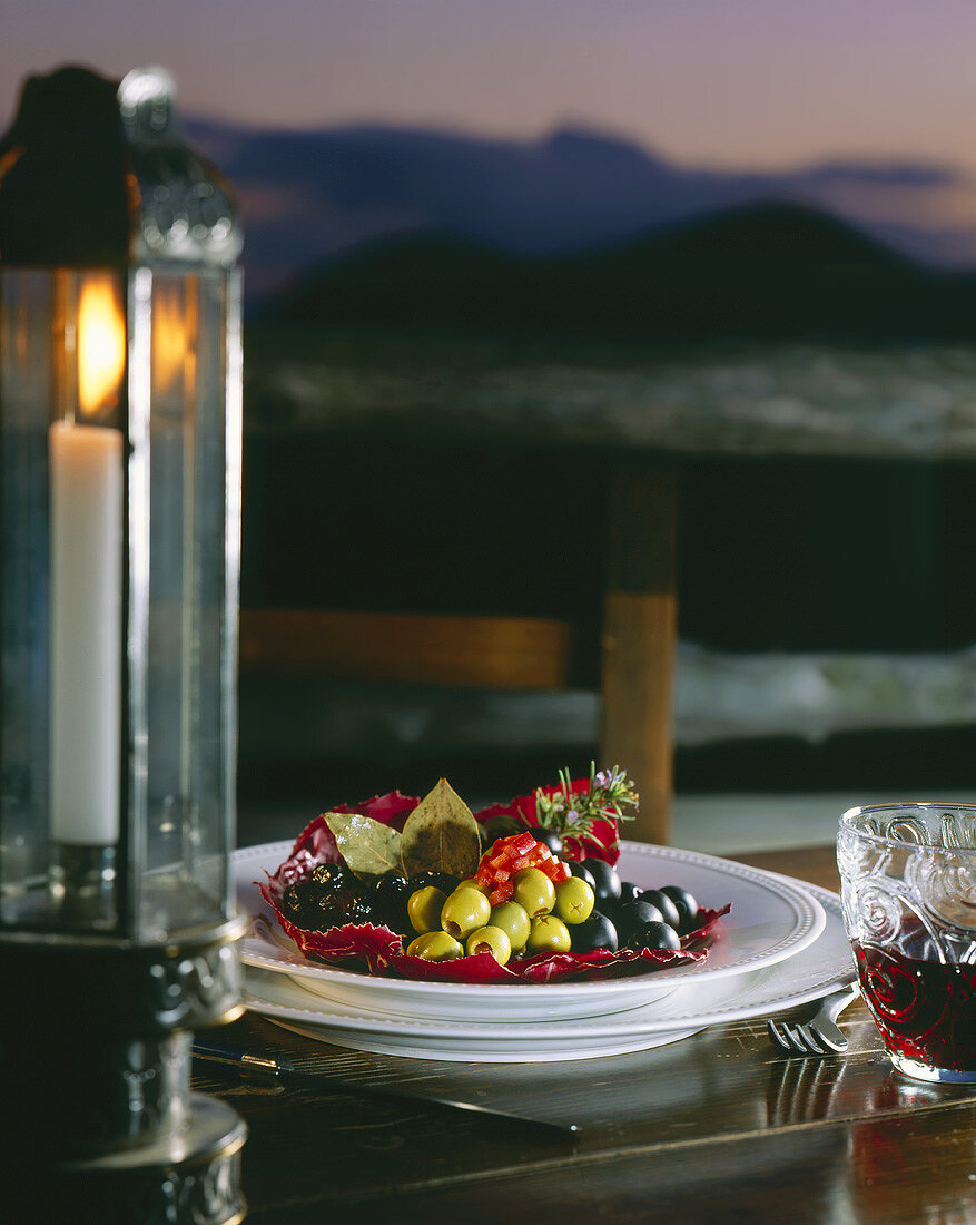 Teller mit Oliven auf gedecktem Tisch am Meer bei Kerzenlicht