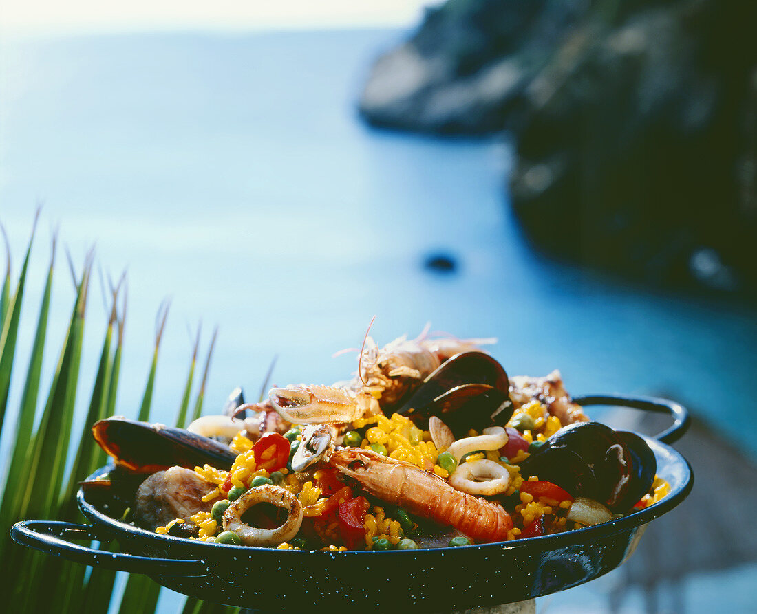Paella in a pan, cliffs and sea in the background
