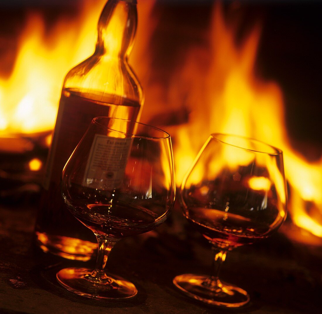 Cognac in Gläsern und in Flasche vor offenem Kamin