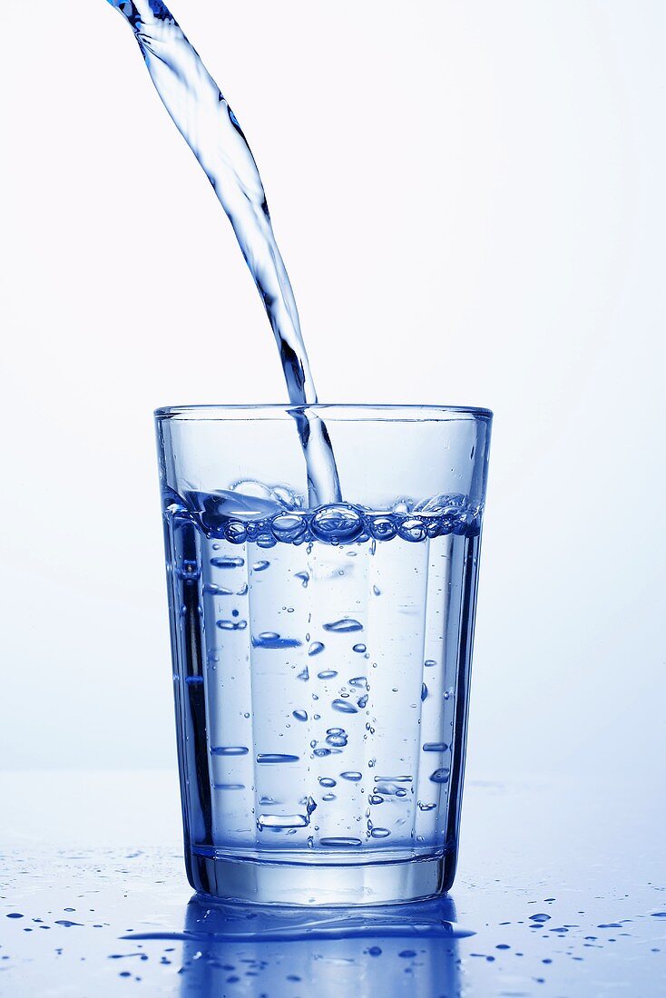 Mineralwasser wird in ein Wasserglas gegossen