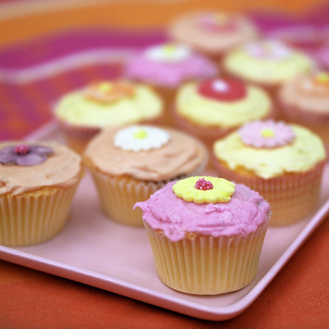 Mehrere bunte Cup Cakes mit Zuckerblüten verziert
