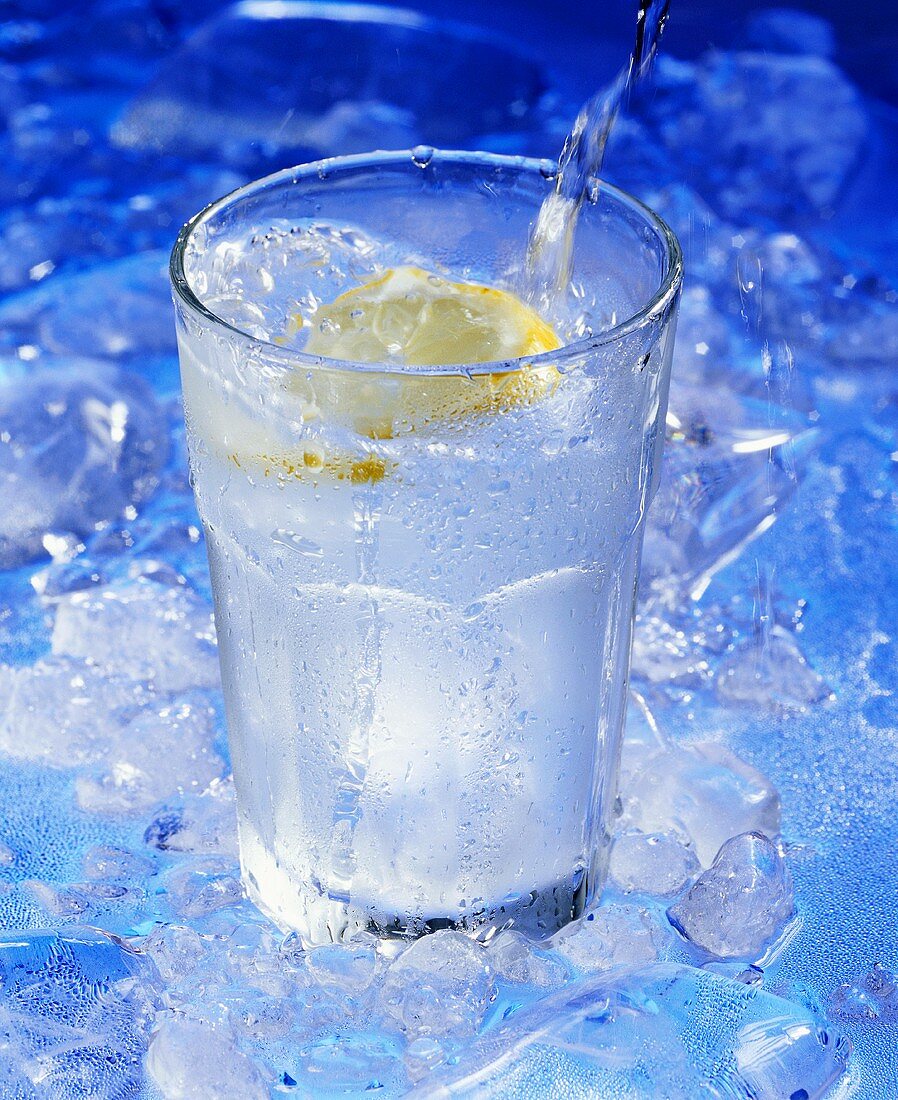 Wasser wird in Glas mit Zitronenschnitz eingeschenkt