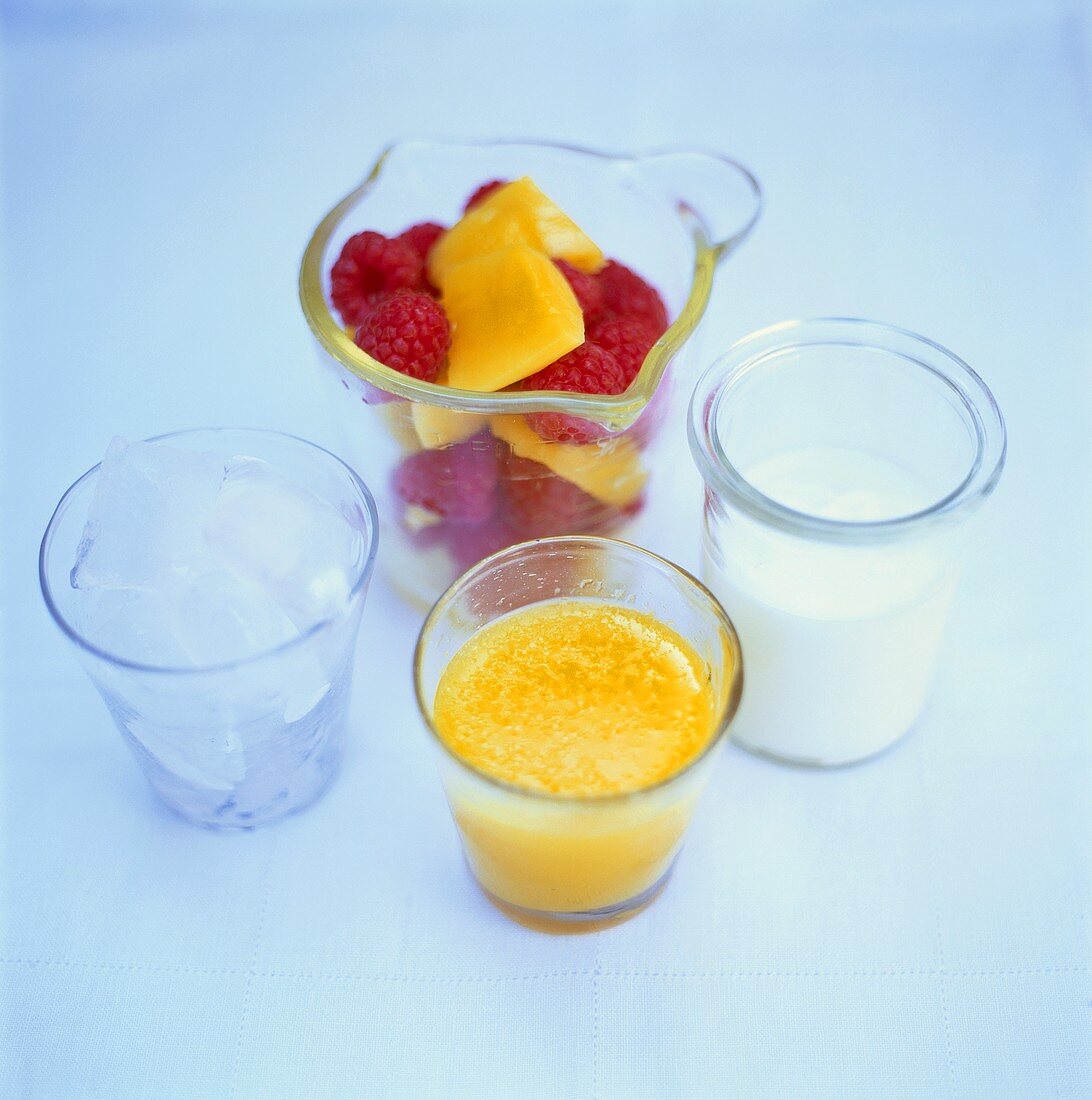 Four glasses filled with mango, raspberries, ice cubes and milk