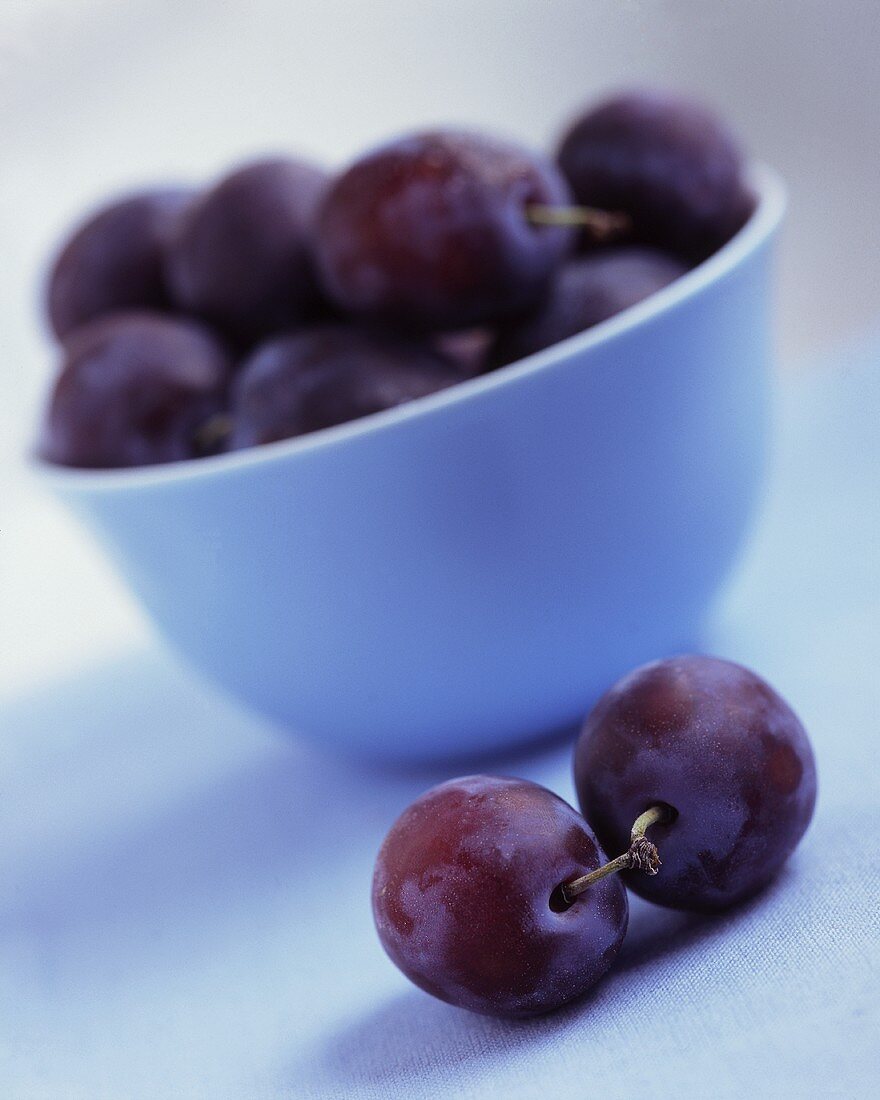 Plums in and in front of a bowl