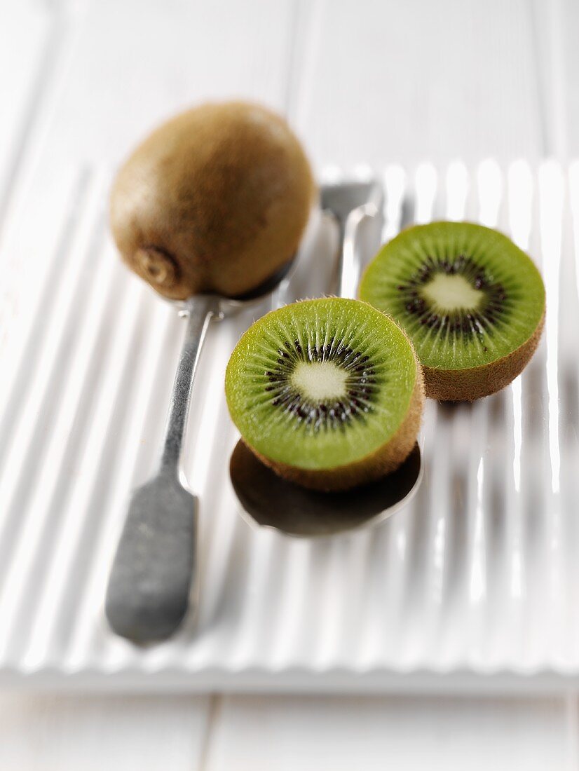One whole and two half kiwi fruits on spoons