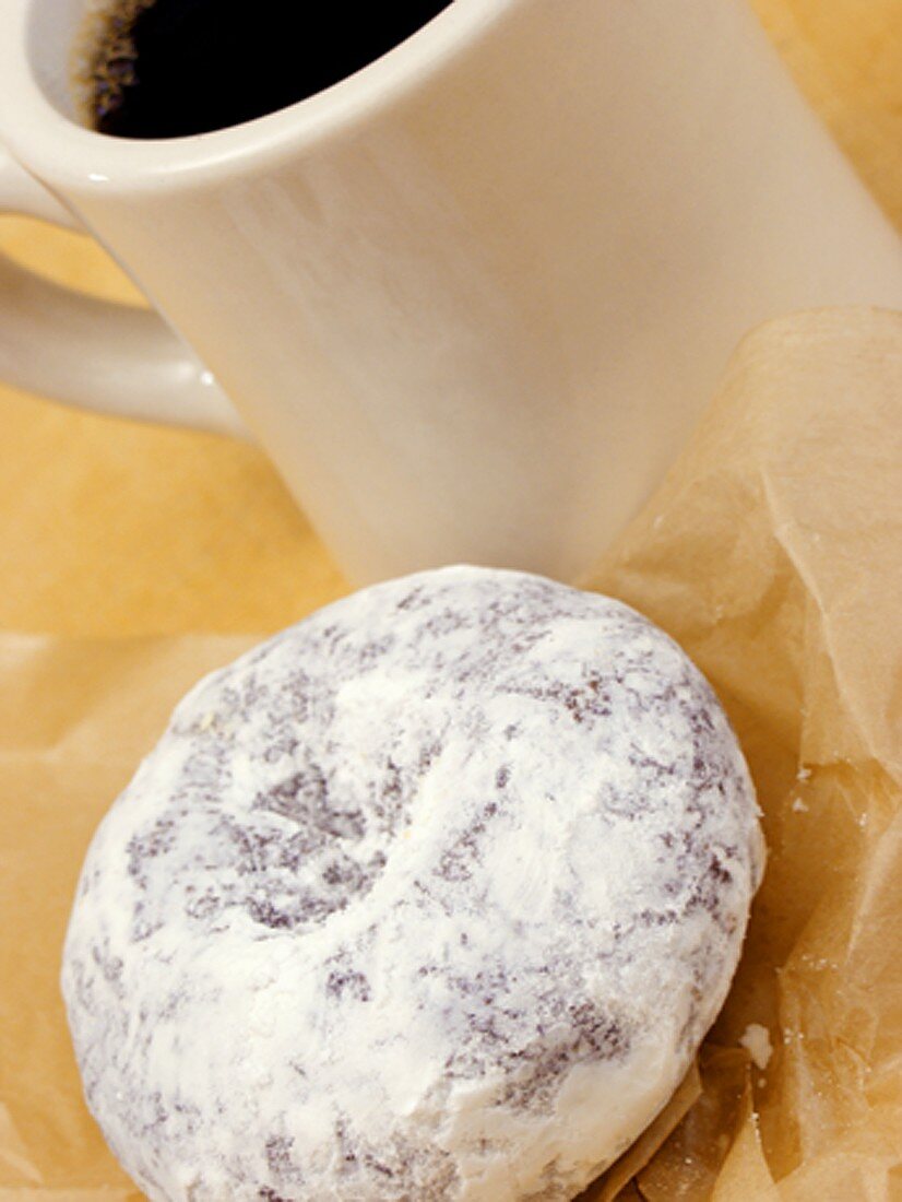 Doughnut mit Puderzucker neben Kaffeetasse